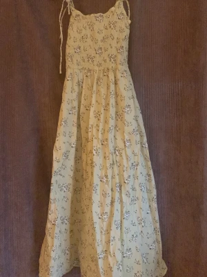 Gul blommig långklänning H&M - Söt långklänning från H&M i ljusgul nyans med småblommigt mönster. Klänningen har smock upptill, tunna axelband med knyt och en luftig passform. Perfekt för varma dagar och sommarhäng.
