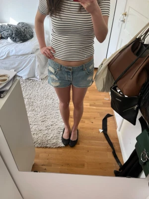 Blå slitna jeansshorts med låg midja - Säljer ett par blå jeansshorts med låg midja och slitna detaljer. Perfekta för varma sommardagar och ger en avslappnad look.
