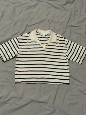 Randig croppad topp från Kappahl - Säljer en croppad topp från Kappahl med svartvita horisontella ränder och krage i offwhite. Toppen har korta ärmar och en avslappnad passform, perfekt för en trendig och chill look.