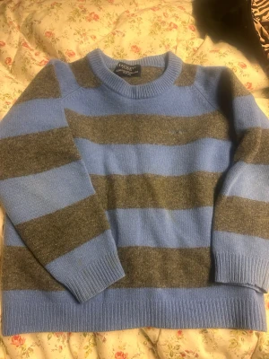 Randig stickad tröja från Hackett barn - Stickad tröja från Hackett London i blått och grått med breda horisontella ränder. Tröjan har rund halsringning och ribbade muddar vid ärmslut och nederkant. Perfekt för en cool och avslappnad stil.