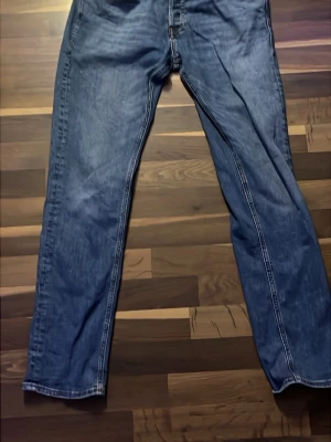 Blå jeans från Jack&Jones - Säljer ett par blå jeans från Jack&Jones med rak passform och klassisk femficksdesign. Jeansen har tydliga sömmar och en lätt tvättad finish som ger en cool och avslappnad stil. Perfekta för dig som gillar enkel och tidlös denim. Storlek 31/32