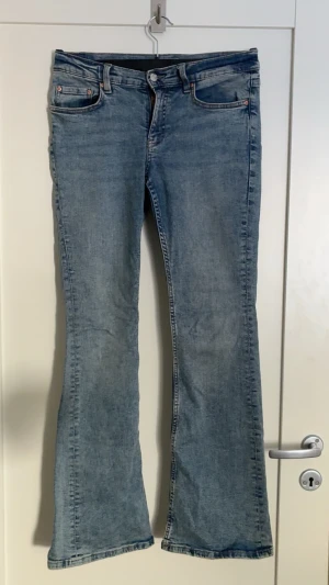 Ljusblå bootcut jeans - Säljer ett par ljusblå bootcut jeans med klassisk femficksdesign och normalhög midja. Jeansen har utsvängda ben och är tillverkade i ett mjukt denimtyg. Perfekta för en avslappnad och trendig look.
