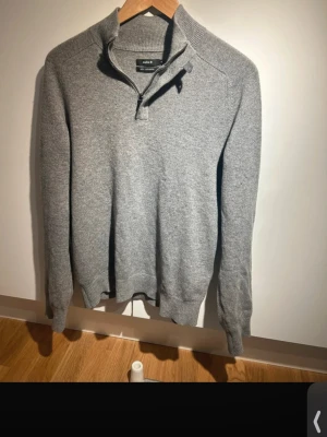 Grå kashmirtröja med halv dragkedja - Mjuk och stilren grå stickad tröja från Celio i 100% kashmir. Tröjan har en halv dragkedja vid halsen och ribbade muddar vid ärmslut och nederkant. Perfekt för dig som gillar en clean och klassisk look.