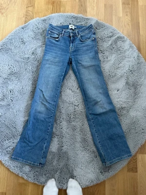 Blå bootcut jeans från lager 157 - Snygga blå bootcut jeans från lager 157 med klassisk femficksdesign och silverfärgade detaljer på bakfickorna. Jeansen har normalhög midja och är tillverkade i denim med lätt stretch för skön passform.