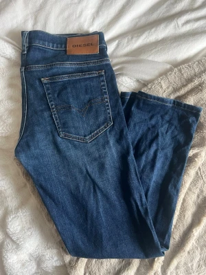 Blå jeans från Diesel - Säljer ett par klassiska blå jeans från Diesel med fem fickor och snygga kontrastsömmar. Jeansen har rak passform och är tillverkade i slitstarkt denim-material. Perfekt för dig som gillar en tidlös och cool look.