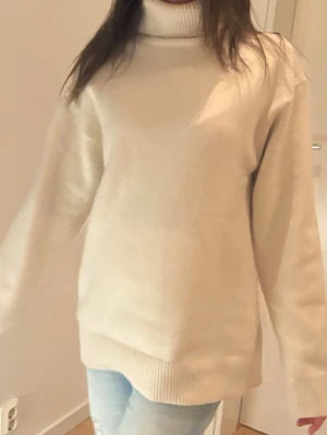 Beige polotröja i stickat material - Mysig beige stickad polotröja med hög krage och avslappnad passform. Tröjan har långa ärmar och ribbade muddar vid ärmslut och nederkant. Perfekt för kyliga dagar och enkel att matcha med jeans eller kjol.