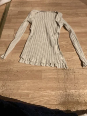 Ljusgrå ribbad långärmad tröja - Säljer en ljusgrå ribbad tröja med lång ärm och rund hals. Tröjan har en figurnära passform och är tillverkad i ett mjukt, stretchigt material. Perfekt att styla med jeans eller kjol för en clean look.