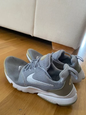 Grå Nike sneakers mesh - Snygga grå Nike sneakers med vit sula och vit swoosh-logga på sidan. Ovandelen är i ventilerande meshmaterial och skorna har en sportig, låg profil. Perfekta för en avslappnad och trendig stil.