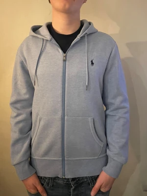 Polo Ralph Lauren ziphoodie ljusblå  - Säljer en riktigt snygg polo Ralph lauren zip hoodie som är knappt använd nästan helt ny använd ca 5 gånger! Så skicket är 9.5/10 skulle ja säga Den är i storlek Small/S och köptes för 2200 i Ralph lauren butik! Hör av dig vid intresse.