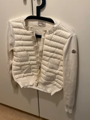 Moncler cardigan  - Snygg unik vit cardiganjacka från Moncler med quiltad framsida och 4 fickor. Jackan har  Ärmarna stickade och vänster ärm har Moncler-logga. Perfekt för lager på lager och streetstyle. Kvitto finns