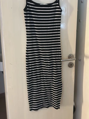 Randig svartvit långklänning - Snygg långklänning med svarta och vita horisontella ränder. Ärmlös modell med rund halsringning och kroppsnära passform. Perfekt för en stilren och avslappnad look.