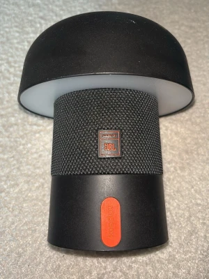 JBL x Kooduu trådlös högtalare - Snygg trådlös högtalare från JBL i samarbete med Kooduu. Högtalaren är svart med textilklädd mittdel och har en inbyggd lampa upptill. Modern design med rundad form och orange detalj. Perfekt för att ta med sig eller ha hemma för schysst ljud och belysning.💕💕