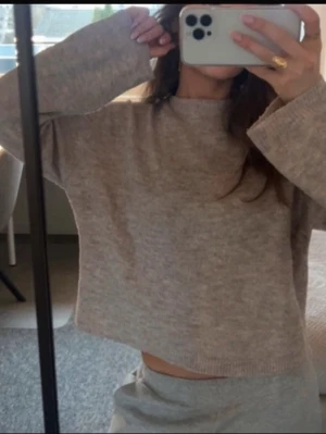 Beige croppad stickad tröja - Mysig croppad stickad tröja i beige med rund hals och långa ärmar. Tröjan har en avslappnad passform och ribbade muddar vid ärmslut och nederkant. Perfekt för lager på lager och chill vardagsstil.