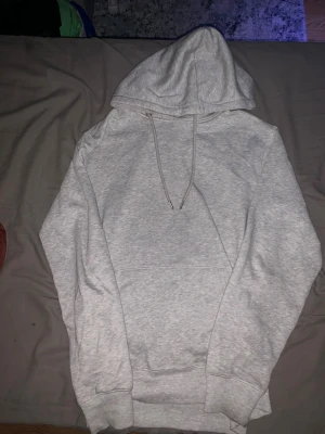 Ljusgrå hoodie från 157 - En stilren ljusgrå hoodie från 157 med klassisk huva och dragsnören. Hoodien har en stor magficka och ribbade muddar vid ärmslut och nederkant. Perfekt för en avslappnad och trendig look.