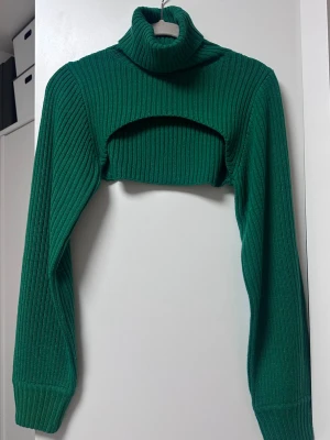 Grön cropped stickad polotröja - Trendig grön ribbstickad cropped polotröja med långa ärmar och hög krage. Perfekt för lager-på-lager och ger en cool vibe till din outfit. Materialet är mjukt och stretchigt för extra komfort.