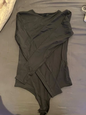 Svart långärmad body från Amisu - Säljer en svart långärmad body från Amisu. Bodyn har rund halsringning och är tillverkad i ett mjukt, stretchigt material som sitter skönt mot kroppen. Perfekt att styla med jeans eller kjol för en clean look.