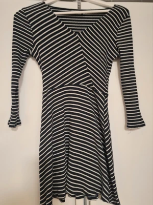 Marinblå/vit  randig klänning  - Snygg marinblå/vit klänning. Klänningen har trekvartsärm och v-ringning, samt en lätt utställd kjol. Perfekt för dig som gillar en enkel men trendig stil. Passar även XS