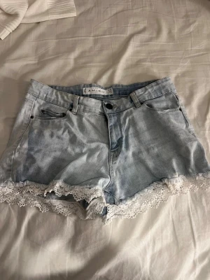 Ljusblå jeansshorts med spetskant - Snygga ljusblå jeansshorts från Amisu med vit spetskant längst ner. Klassisk femficksmodell med knapp och dragkedja framtill. Perfekta för sommaren och ger en söt touch till din outfit.