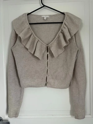 Beige kofta med volangkrage - Snygg beige stickad kofta med volangkrage och pärlknappar framtill. Stolek S, skriv gärna vid frågor!!🩷