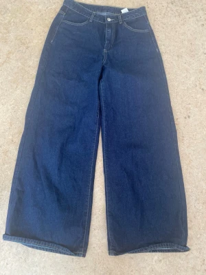 Mörkblåa wide leg jeans - Säljer ett par mörkblåa jeans med breda ben och klassisk femficksdesign. Jeansen har hög midja och kontrastsömmar. Perfekta för dig som gillar en avslappnad och trendig stil. Materialet är denim i bomull.