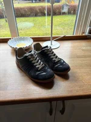 Svarta sneakers med mockadetaljer - Snygga svarta sneakers med beige sula och vita skosnören. Skorna har en mix av mocka och läder på ovandelen, vilket ger en schysst kontrast. Klassisk låg modell som passar till det mesta. Perfekt för dig som gillar stilrena och tidlösa sneakers.