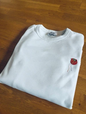 Vit hoodie från Acne Studios - Snygg vit hoodie från Acne Studios med broderad röd ballong på bröstet. Klassisk passform med rund hals och ribbade muddar. Perfekt för dig som gillar stilrena plagg med en unik detalj.