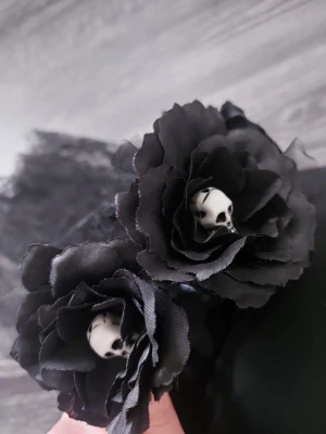 Svart diadem med rosor och dödskallar - Unikt svart diadem dekorerat med stora tygrosor och små vita dödskallar i mitten av blommorna. Diademet har även svart spets som ger en extra dramatisk look. Perfekt för dig som gillar alternativ stil eller vill sticka ut lite extra.