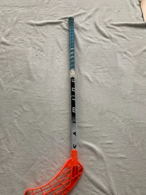 Salming innebandyklubba blå/orange - Säljer en innebandyklubba från Salming med blått grepp, svart och vitt skaft samt orange blad. Klubban har ett lätt böjt blad i plast och greppet är lindat för bra kontroll. Perfekt för dig som vill ta ditt spel till nästa nivå.