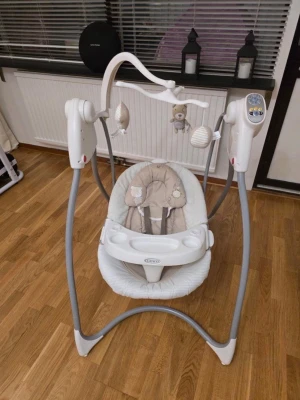 Elektrisk babysitter från Graco - Elektrisk babysitter i vitt och beige med grå stativ från Graco. Utrustad med gungfunktion, musikpanel och lekbåge med mjuka hängande figurer. Sitsen har mjuk stoppning och säkerhetssele. Perfekt för att underhålla och lugna små barn.