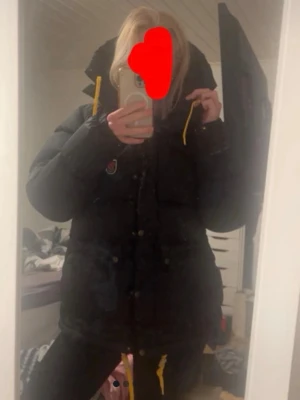 Svart Fjällräven Expedition dunjacka - Säljer en svart Fjällräven Expedition dunjacka med gula dragskor. Jackan har en klassisk puffy design och Fjällräven-logga på bröstet. Tillverkad i slitstarkt material och fylld med dun för maximal värme under kalla vinterdagar. Är storlek M men passar mig som bär storlek xs-s. Kan mötas upp i Stockholm! 🥰