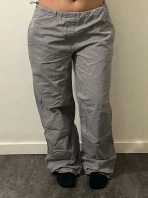 Grå or med dragsko - Säljer ett par grå cargobyxor med avslappnad passform och dragsko i midjan. Byxorna har fickor på sidorna och baktill samt resår i benslut. Tillverkade i ett mjukt och lätt material som ger en skön streetwear-look.