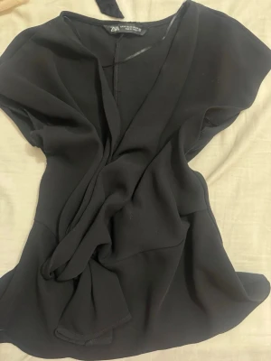 Zara viral omelett top - Snygg svart omlottklänning från Zara med v-ringning och korta ärmar. Klänningen har ett knyt i midjan som ger en smickrande siluett och är tillverkad i ett mjukt, lätt material. Perfekt för dig som gillar stilrena och enkla plagg.  Köpt för 350 och den säljs inte mer!