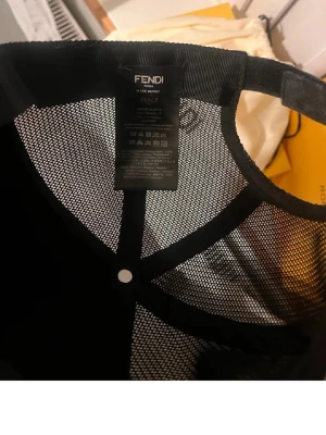 Svart meshkeps - Säljer en svart keps från Fendi med meshpaneler som ger en luftig och sportig känsla. Kepsen har justerbar rem bak och klassisk böjd skärm. Perfekt för dig som vill ha en stilren accessoar med exklusiv känsla och diskret logga.
