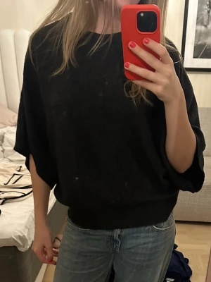 Svart trekvartsärmad tröja - Säljer en svart oversized stickad tröja med bred passform och halvlånga ärmar. Tröjan har rund halsringning och ribbade muddar vid hals och nederkant. Perfekt för en avslappnad och trendig look.