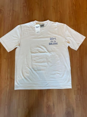 Vit t-shirt från Gallery Dept. - Vit t-shirt från Gallery Dept. med trycket 'DÉPT. de la GALERIE' i blått. Aldrig använd fortfarande med lapp på, skit fin till sommaren och även färgglad, den passar XXL/XL.