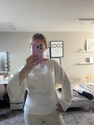 Vit blus med vida ärmar och knytning - Vit satin blus med vida långärmar och snygg knytning i ryggen. Lappen är kvar. 