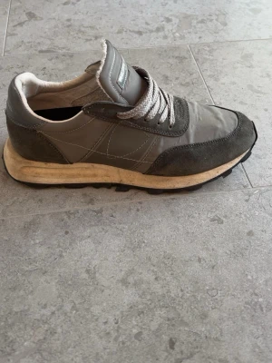Grå sneakers med mockadetaljer - Säljer ett par grå sneakers från Philippe Model med snygga mockadetaljer och gråa skosnören. Skorna har en beige sula och klassisk retroinspirerad design. Ovandelen är i en mix av textil och mocka vilket ger en schysst kontrast och streetkänsla. Använda under våren och var väldigt bekväma. Säljer pågrund av att det har blivit för små. Nypris 2499. Pris går att diskutera 