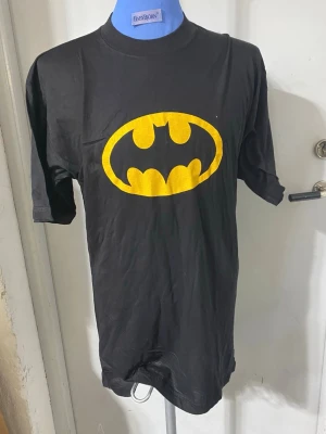 Svart Batman t-shirt  - Cool svart t-shirt med det klassiska Batman-loggan i gult på bröstet. T-shirten har rund hals och korta ärmar, perfekt för dig som gillar superhjältar och vill sticka ut med en ikonisk look. Finns L och XL i storlek kvar, helt ny , 129kr /st , samma frakt 