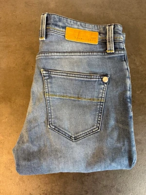 Ljusblå slim fit jeans från Tramarossa W34 - Snygga ljusblå slim fit jeans från Tramarossa med klassisk femficksdesign och guldfärgad patch bak i midjan. Jeansen har en lätt tvättad look och raka ben. Perfekta för en avslappnad och trendig stil. Skriv för mått!