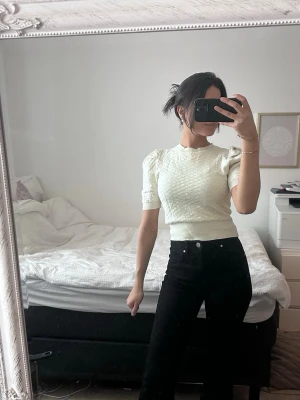 Vit kortärmad topp med struktur - Snygg vit topp med korta puffärmar och strukturerat tyg. Modellen är croppad och har en tight passform som framhäver midjan. Perfekt att styla med höga jeans eller kjol för en trendig look.