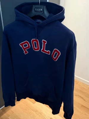 Mörkblå hoodie från Polo Ralph Lauren - Snygg mörkblå hoodie med stor röd och vit POLO-text på bröstet. Klassisk känguruficka framtill och justerbar huva. Perfekt för en avslappnad och sportig stil. Mjuk bomullskvalitet som känns skön mot huden.                Pris går att diskutera!!