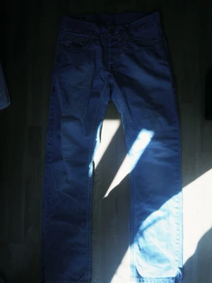 Ljusblå True Religion jeans - Säljer ett par ljusblå jeans från True Religion med klassiska kontrastsömmar och broderade bakfickor. Jeansen har rak passform och detaljerad etikett bak i midjan. Perfekta för dig som gillar streetwear och vill sticka ut med snygga detaljer. Har ett litet hål på baksidan men det går att fixa enkelt.