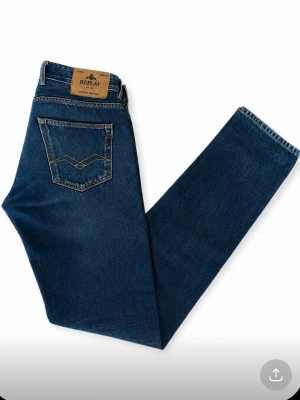 Blå raka jeans från Replay - Snygga blå jeans från Replay med klassisk femficksdesign och raka ben. Jeansen har en mörk tvätt, kontrastsömmar och en läderpatch med Replay-logga bak i midjan. Materialet är denim i bomull. Perfekta för en avslappnad och stilren look.