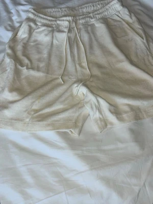 Beige mjukisshorts med dragsko - Ett par beige mjukisshorts i skönt material med resårmidja och dragsko. Shortsen har två sidofickor fram och en bakficka. Perfekta för chill dagar eller när du vill ha det bekvämt. Lite fläckig bara annars är allt bra 