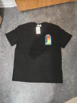 Svart Casa Blanca t-shirt med tryck - Svart t-shirt Casa Blanca med färgglatt grafiskt tryck på bröstet och ryggen. Klassisk passform med rund hals och korta ärmar. Tillverkad i mjuk bomull, perfekt för en trendig och avslappnad stil.
