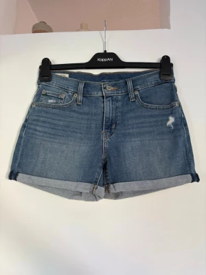 Blå jeansshorts från Levi's - Klassiska blå jeansshorts från Levi's med upprullade benslut och femficksmodell. Läderpatch bak i midjan. Mycket bra skick. Storlek 26🤗