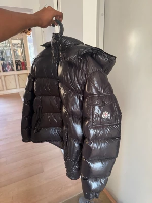 Svart glansig dunjacka från Moncler - Säljer en svart, glansig dunjacka från Moncler med huva och dragkedja framtill.  Maya Moncler köptes från Second Place Trianglen Malmö. Knappt använd. Inga Skam bud !! storlek 6 XL