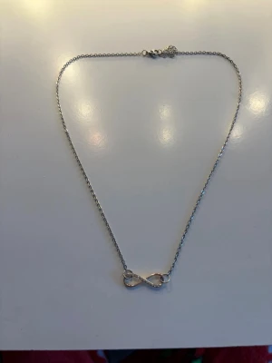 Silverfärgat halsband med infinitysymbol - Snyggt halsband i silverfärg med en tunn kedja och en infinitysymbol som hänge. Symbolen är dekorerad med små glittrande stenar på ena sidan för extra bling. Perfekt accessoar för att lyfta din outfit.