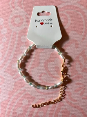 Handgjort pärlarmband med guldkedja - Ett handgjort armband med vita och ljusgröna pärlor, kombinerat med en tunn guldfärgad kedja och karbinlås. Armbandet har en enkel och stilren design som passar perfekt till din vardagsstil.