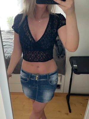 Svart spetsig croppad topp - Säljer en svart croppad topp från MONKI i genombruten spets med omlott och v-ringad hals. Toppen har korta ärmar och sitter tight. Perfekt för sommaren!